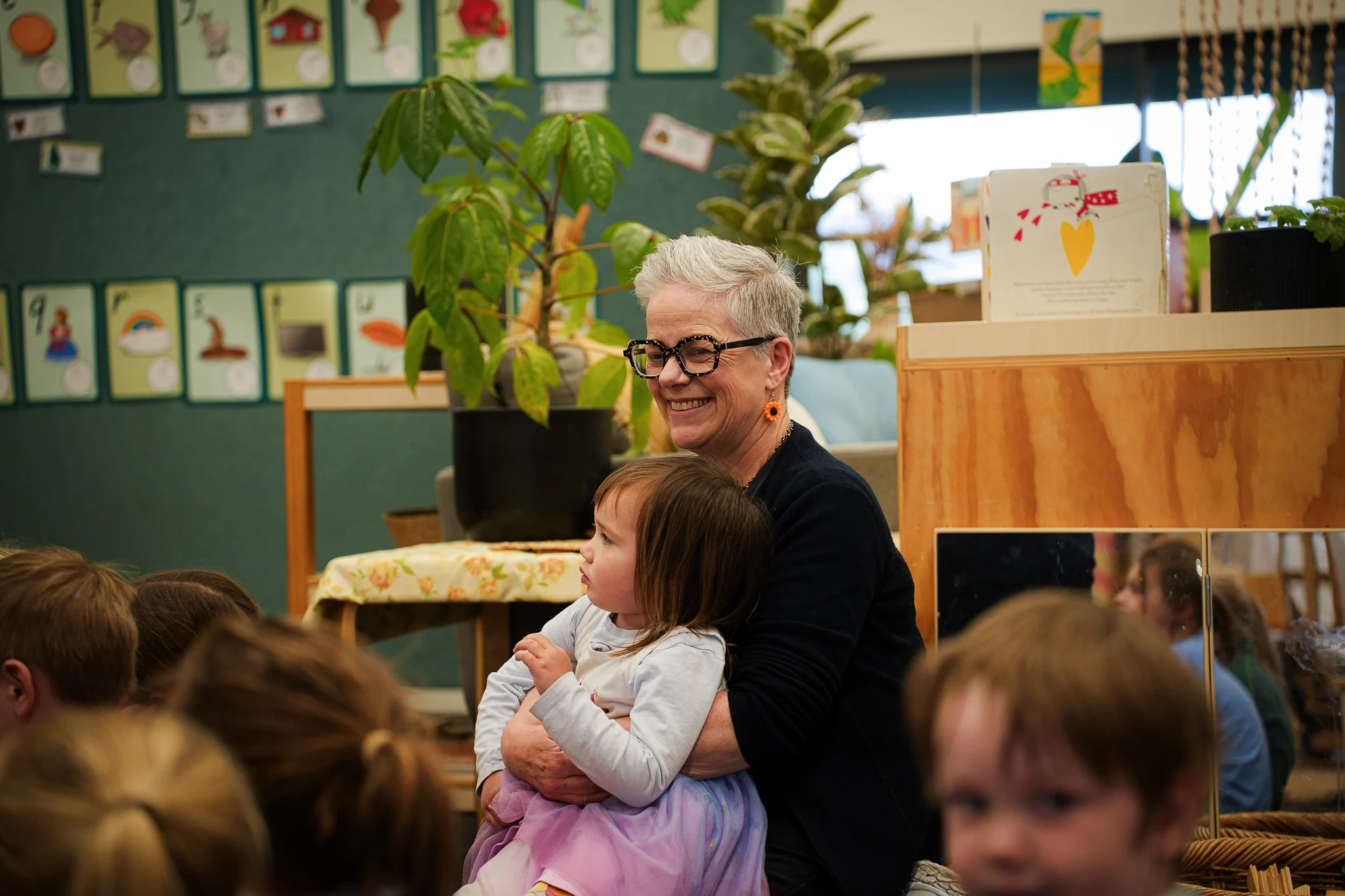 A teacher sits with a young child during group time in the learning space.
