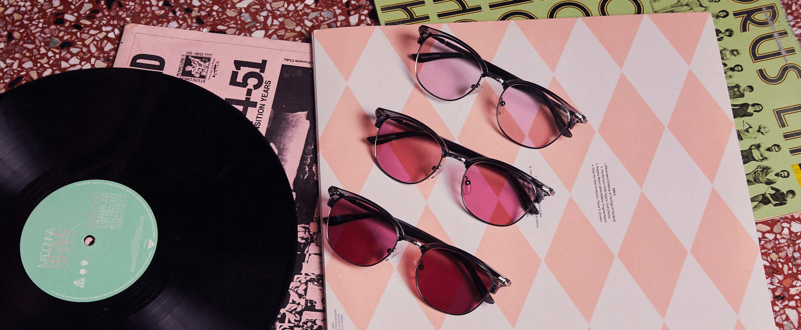 Three Zenni browline frames with FL-41 rose-tinted lenses in graduating depths on a pink argyle record sleeve beside a vinyl record