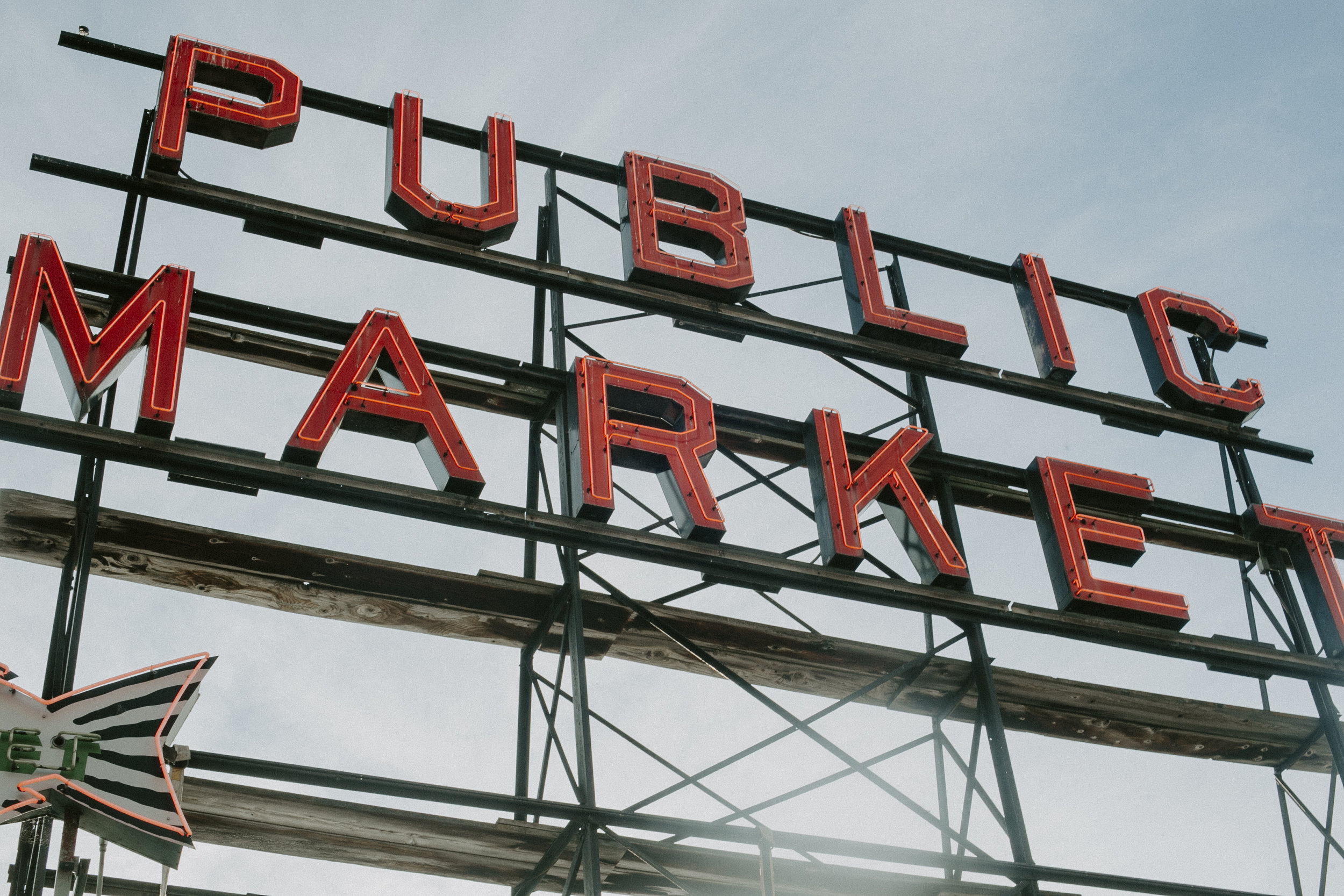 Iconic red neon ‘Public Market’ sign at Pike Place Market, Seattle, framed against a clear blue sky, symbolizing the historic market.