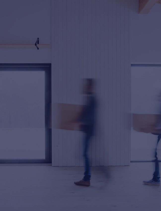 Two blurred people carrying boxes inside a bright, modern home with large windows.