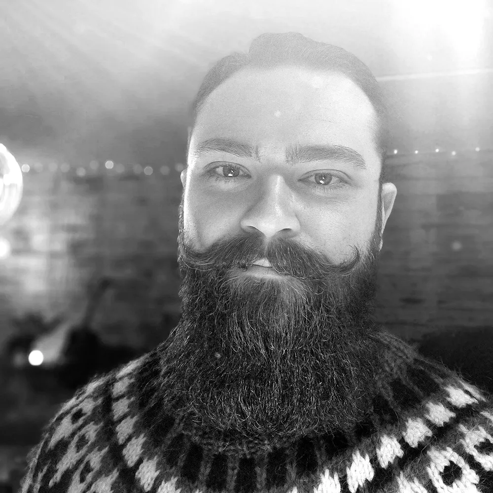 An image of Simon Kamali standing in a field in Iceland with mountains in the background.