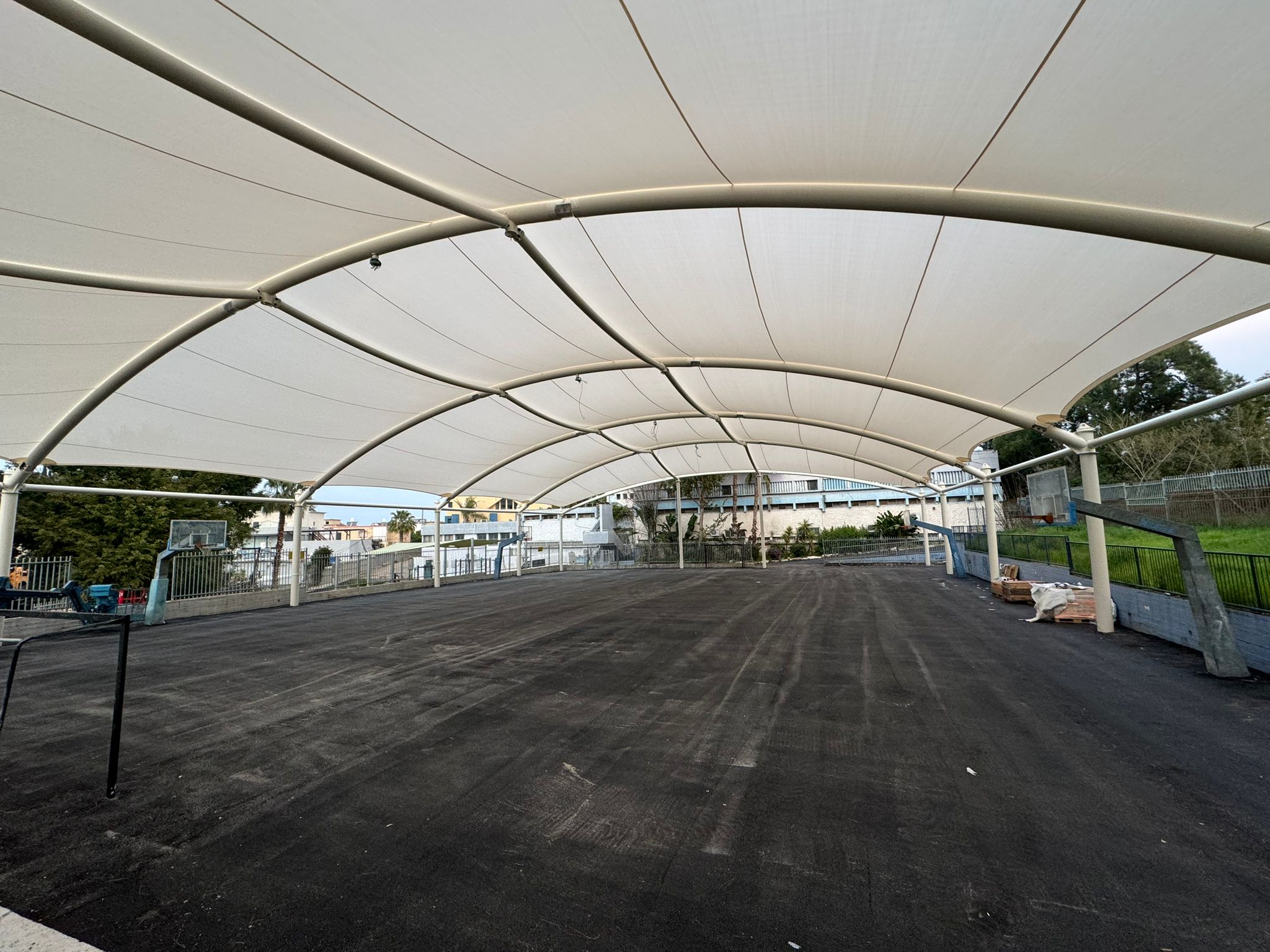 Large outdoor covered area with beige tent roof and black ground surface.