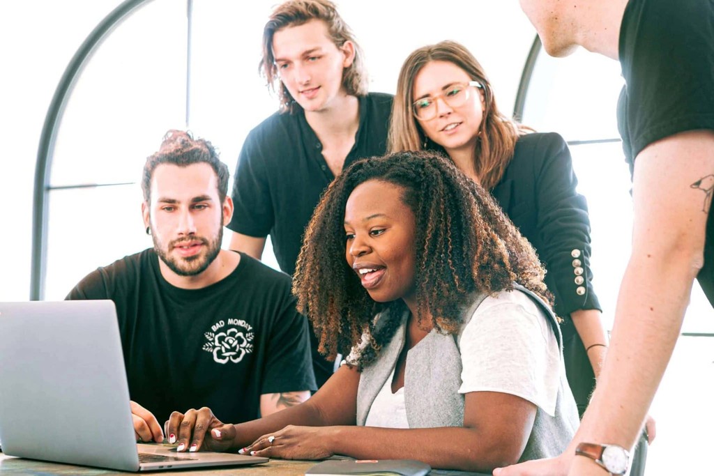 Diverse team collaborating around a laptop in a bright office setting.