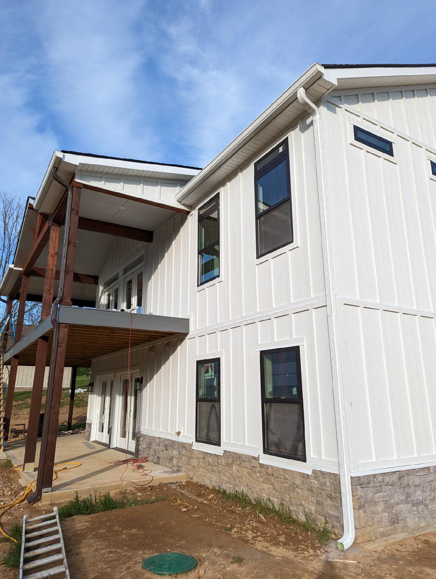 A white house with a spacious porch and deck, showcasing a beautiful exterior design. Gutter installation is also visible.
