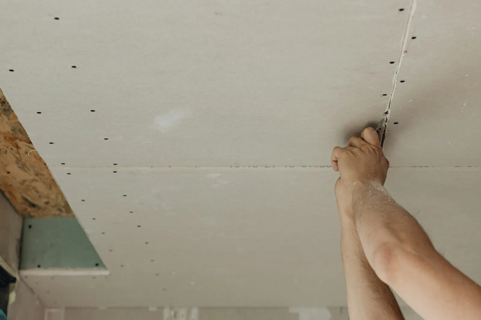 Close-up of hands installing drywall ceiling with screws visible