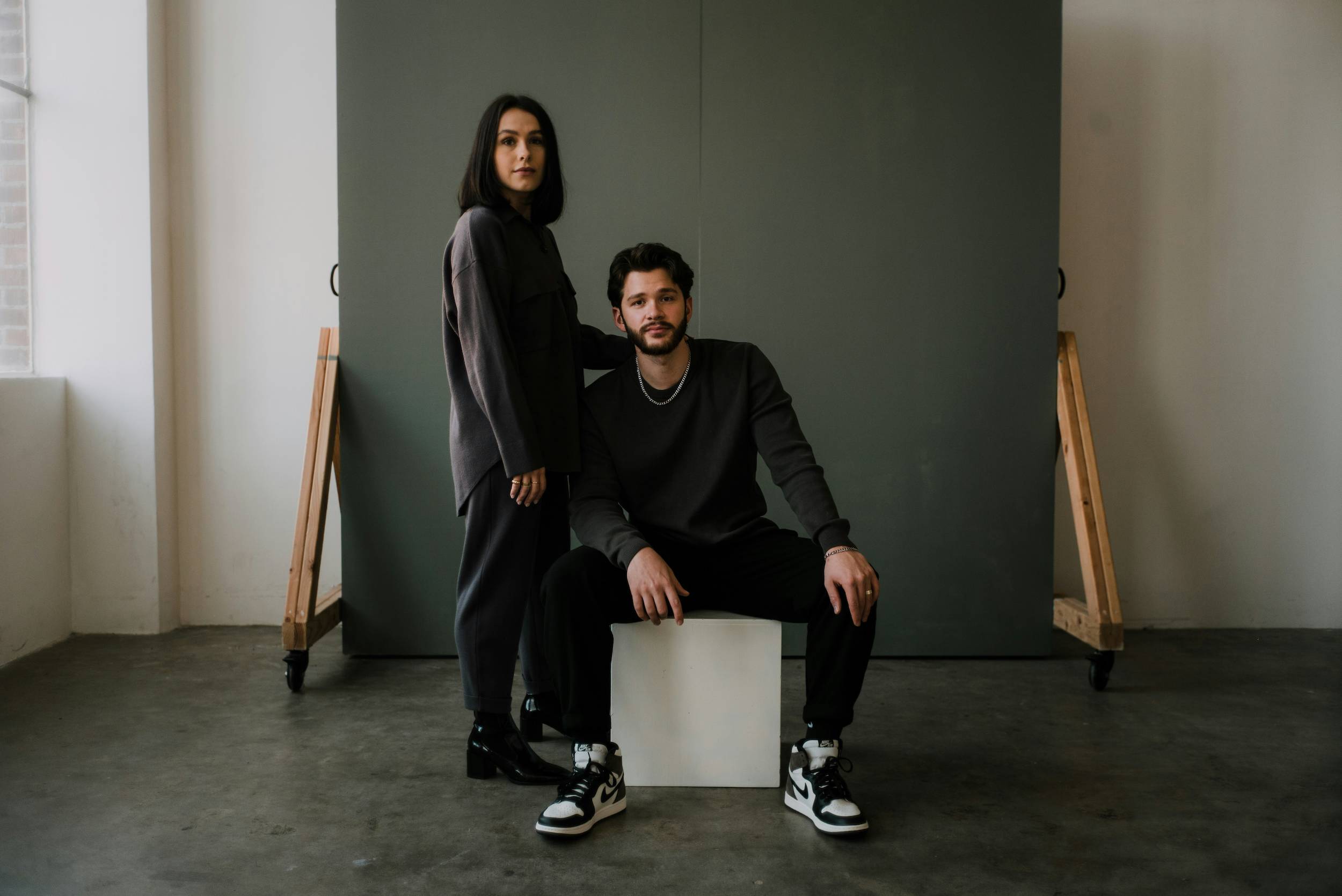 A couple poses creatively on a white square while looking at the camera
