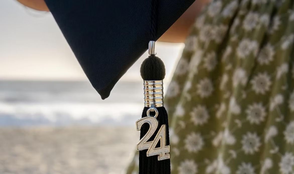 Graduate holding a cap aloft at commencement with classmates in the background.