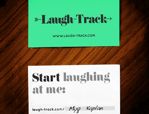 Two business cards rest on a dark wooden surface. The top card is lime green and displays the text "Laugh-Track" with a right-pointing arrow and the website address "www.laugh-track.com". The bottom card is white with the text "Start laughing at me:" in black font. The bottom card also includes the handwritten text "Myg Kaplan" and a slash symbol.