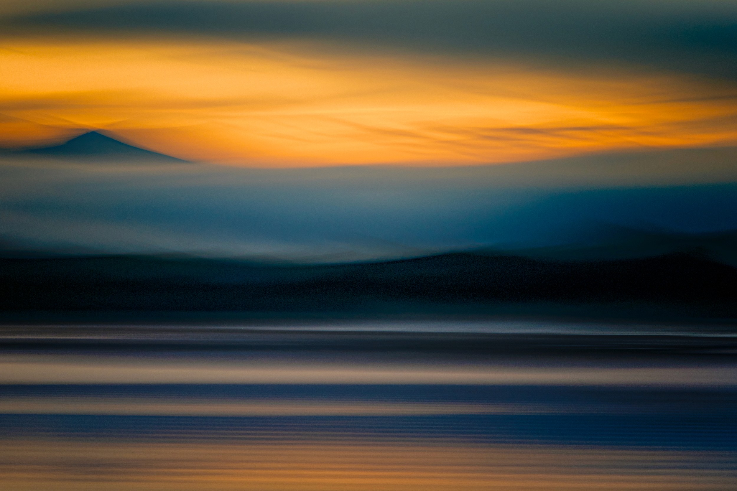 Mountain silhouette layered in warm twilight hues with streaked motion blur