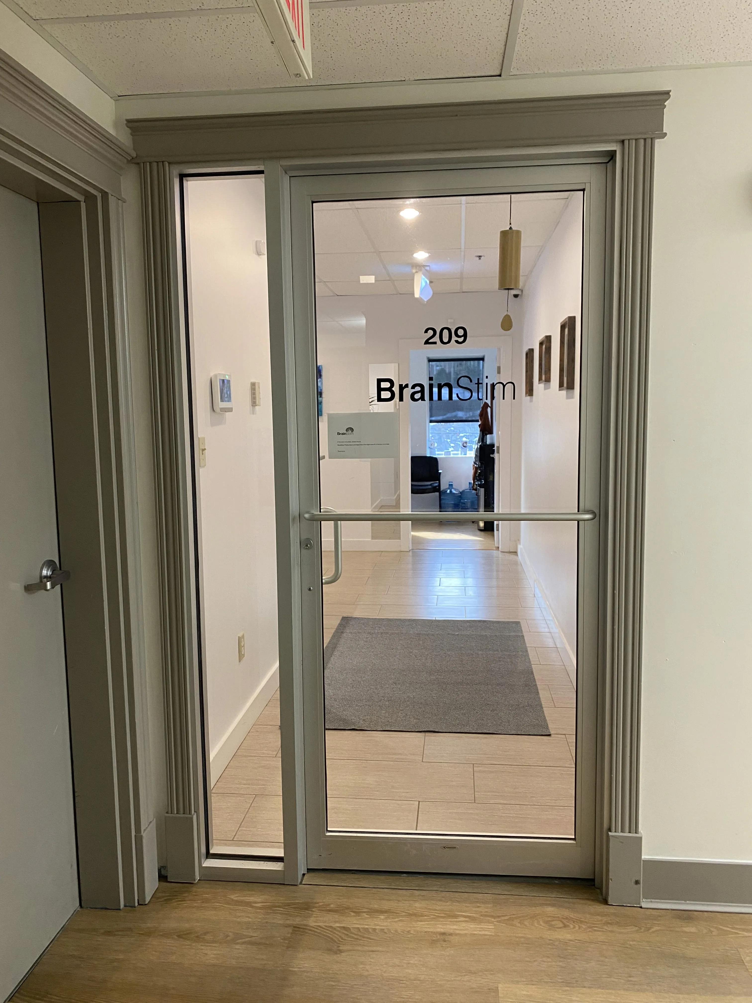 Glass entrance door to Suite 209 displaying the BrainStim logo, with a hallway and reception area visible inside