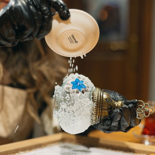 Isang kalahok ang nagbubuhos ng maliliit na puting bato sa isang mosaic na lampara na ginagawa.