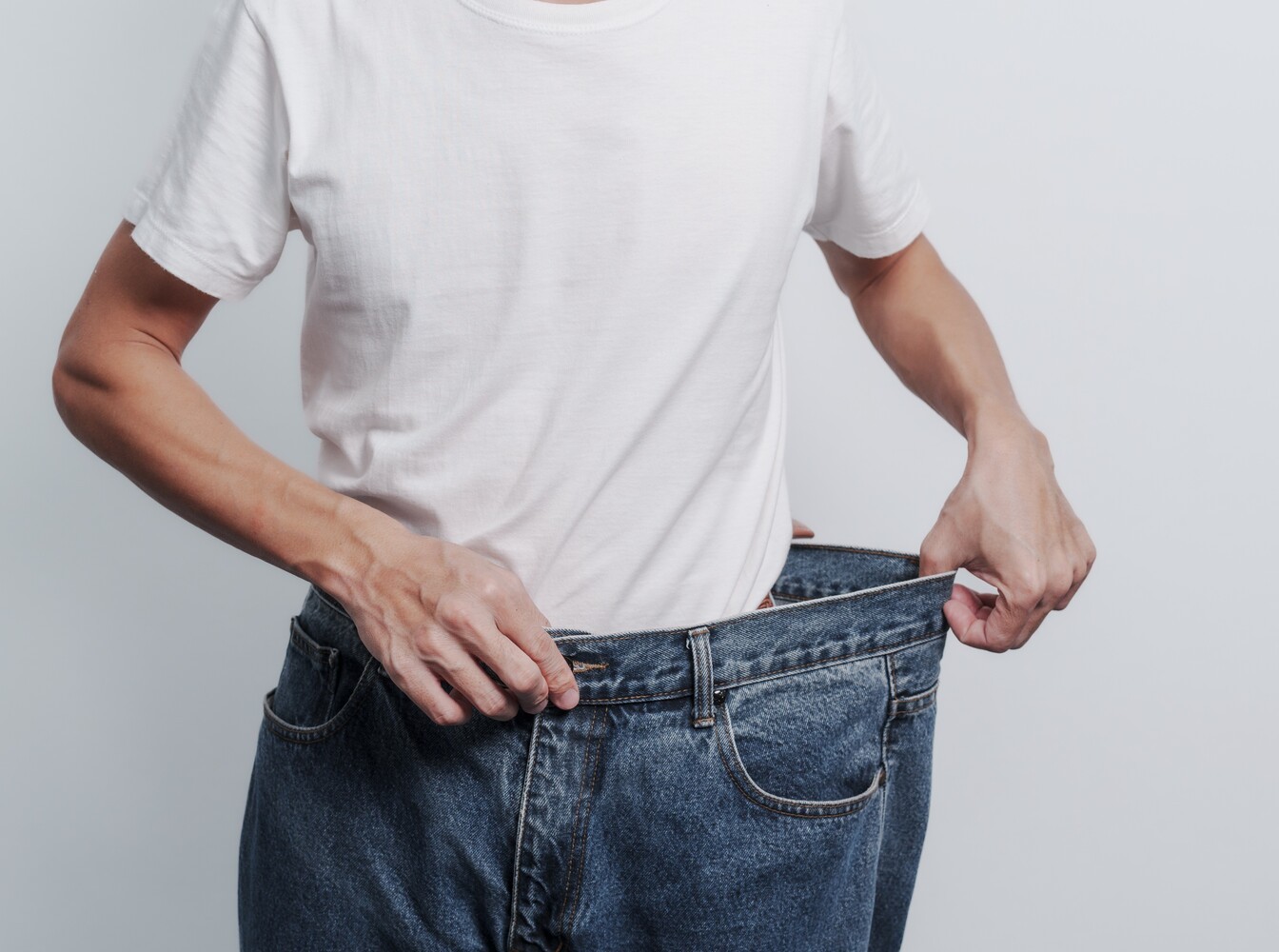 man trying on an old pair of jeans to check his fat loss results, showing the StairMaster is good for weight loss