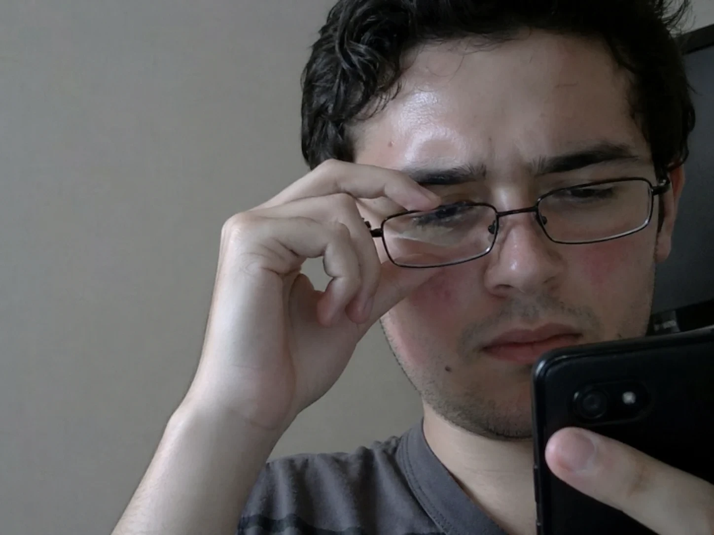 Man wearing glasses looking at phone indoors.