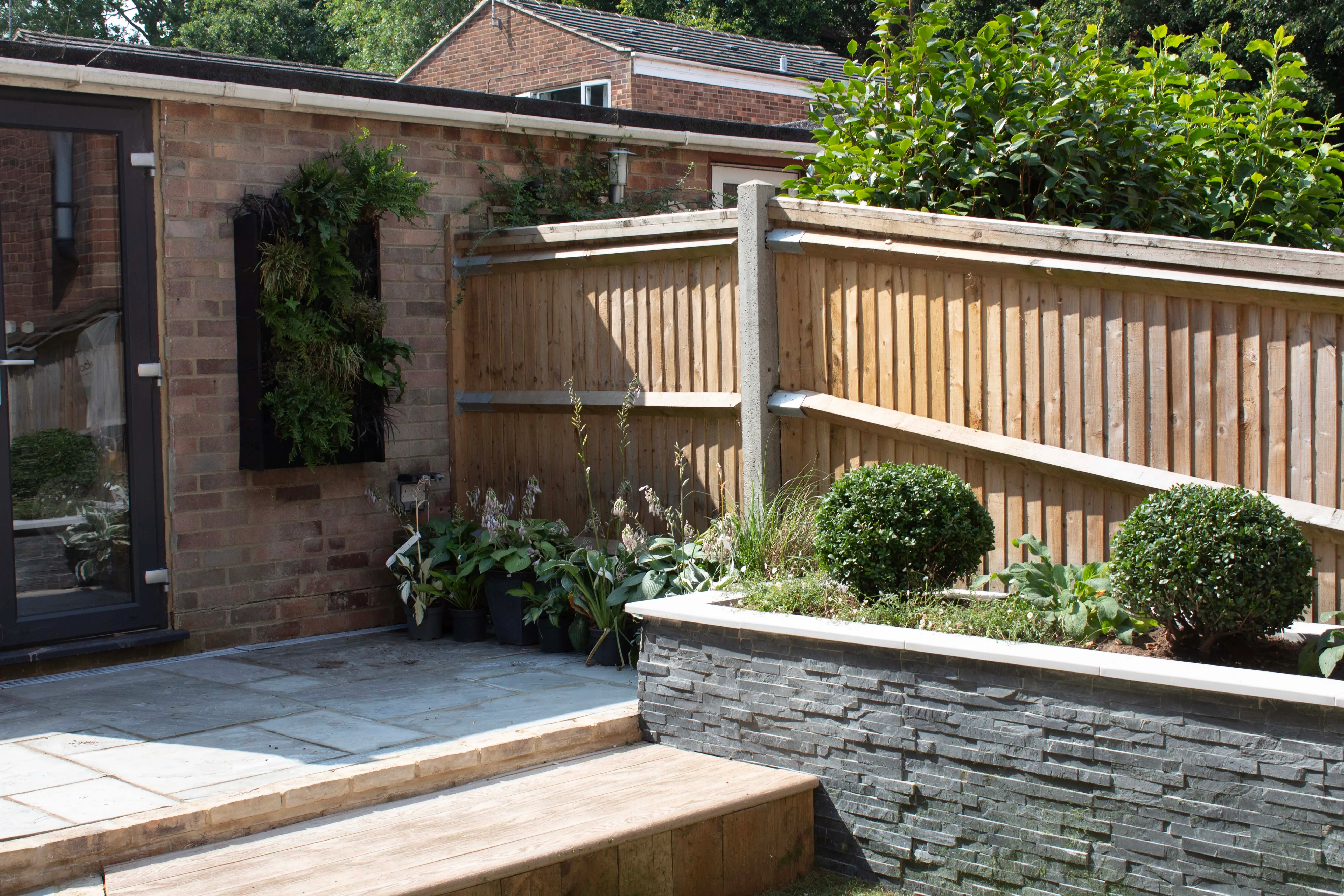 A well-maintained garden featuring a stone path, wooden fence, and green shrubs amidst a sunny outdoor setting.