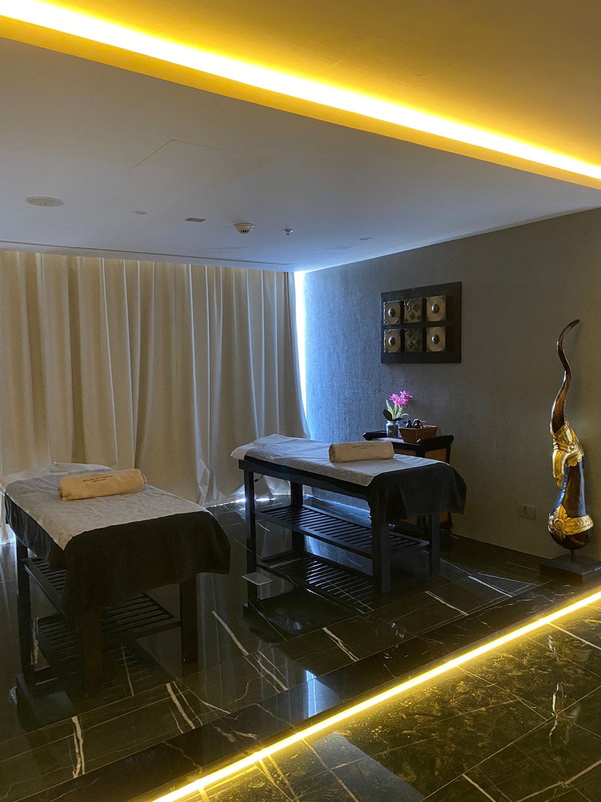 A luxurious indoor spa area with a pool, lounge beds, and a breathtaking view of a city skyline at sunset. The golden lighting enhances the warm and tranquil atmosphere, creating a perfect relaxation retreat.