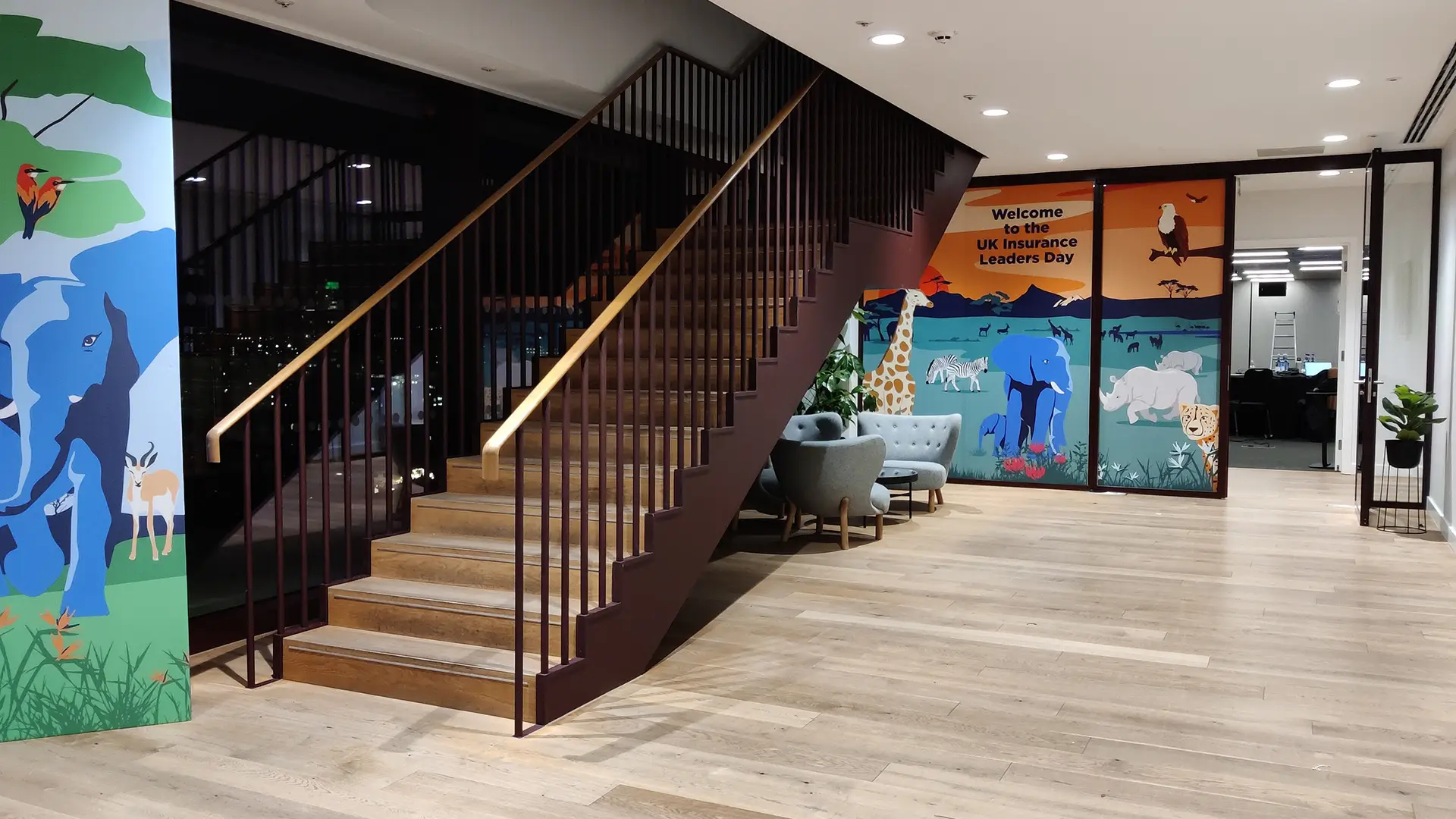 Interior view of the Bupa Strategy Cascades venue, showing a modern staircase, lounge seating, and illustrated wall graphics welcoming attendees to the UK Insurance Leaders Day.