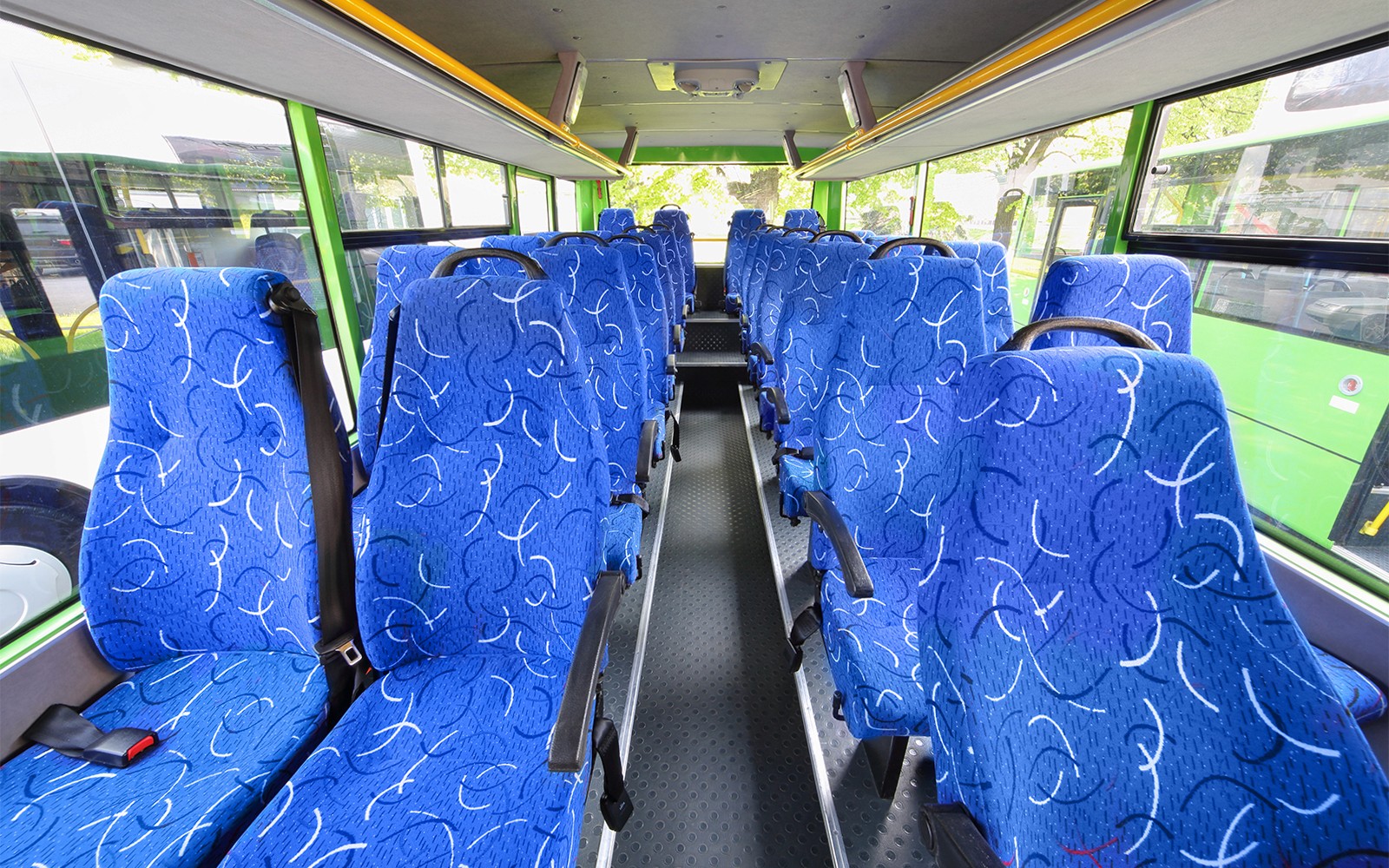 Kursi bermotif biru di dalam bus tur dengan jendela besar.