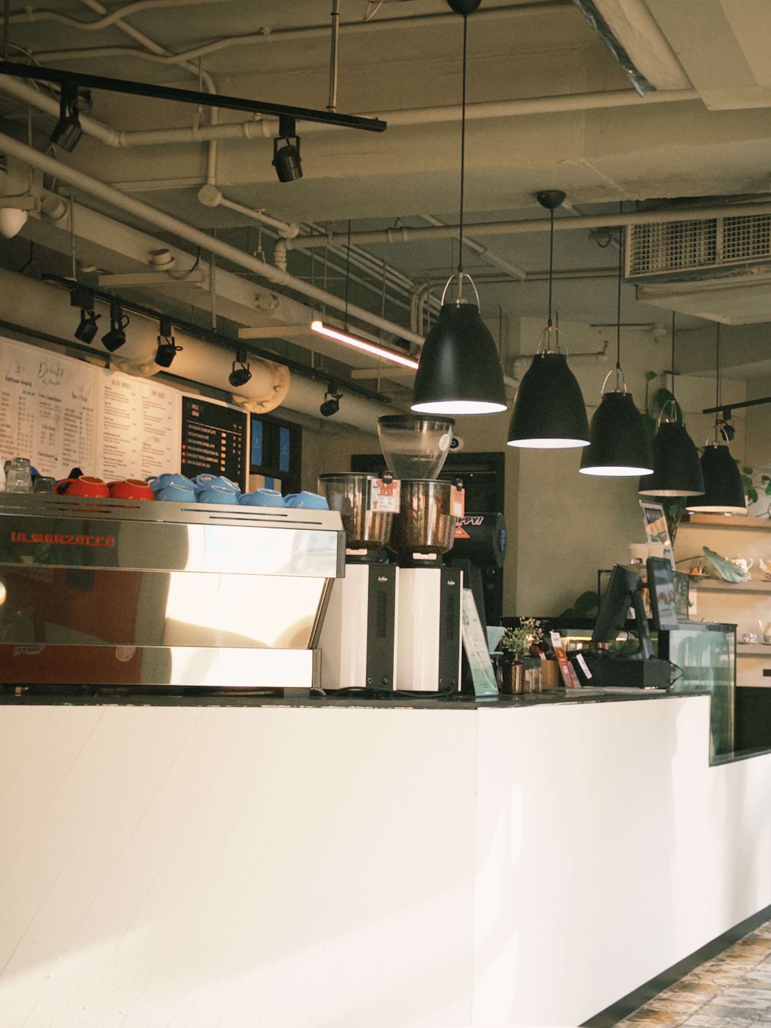 an industrial style cafe with a row of hanging lights and spotlights focused on the menu wall