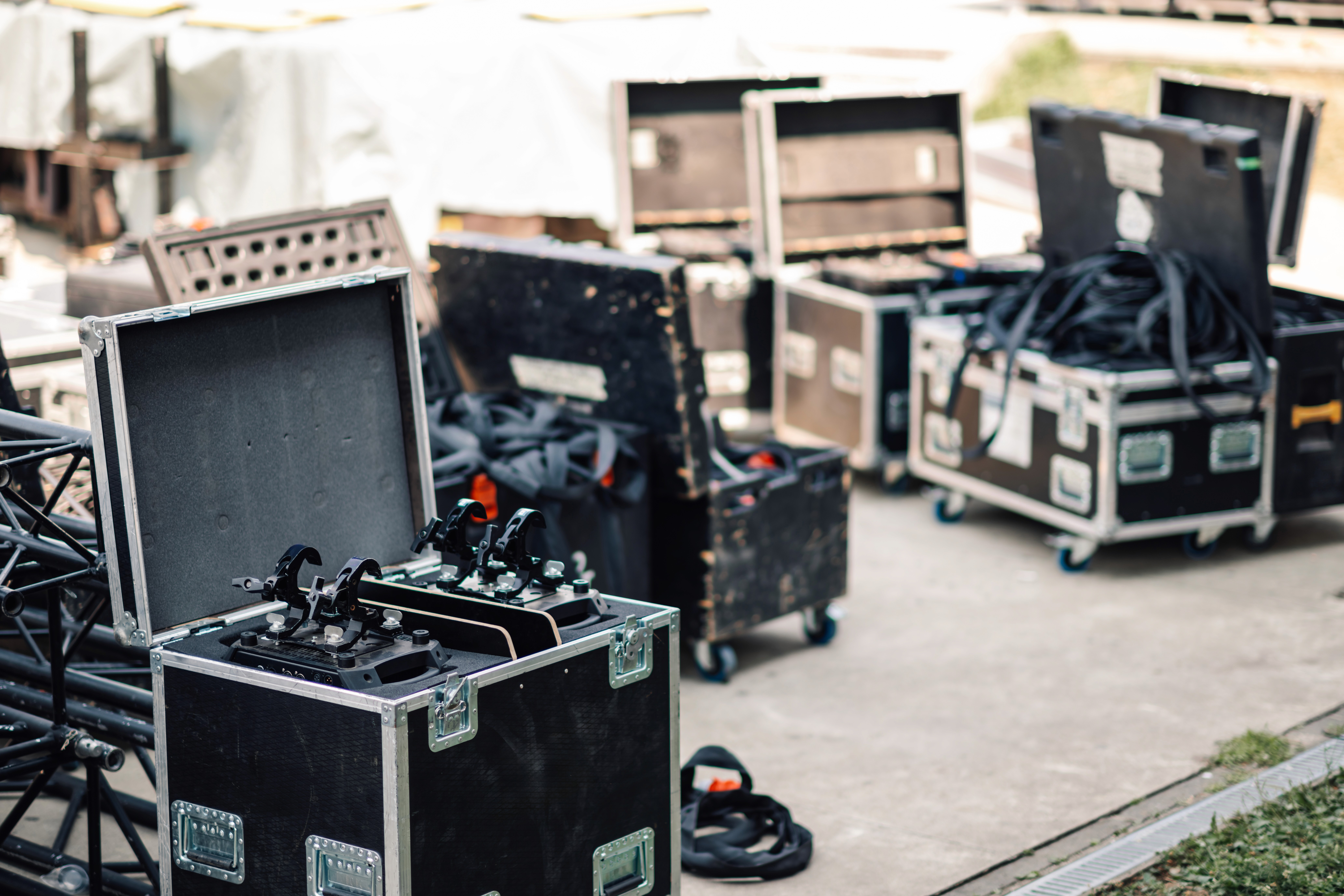 Mehrere offene und geschlossene schwarze Transport- und Flightcases stehen im Freien; darin befinden sich Bühnentechnik, Kabel und Halterungen, die auf den Aufbau einer Veranstaltung hindeuten.