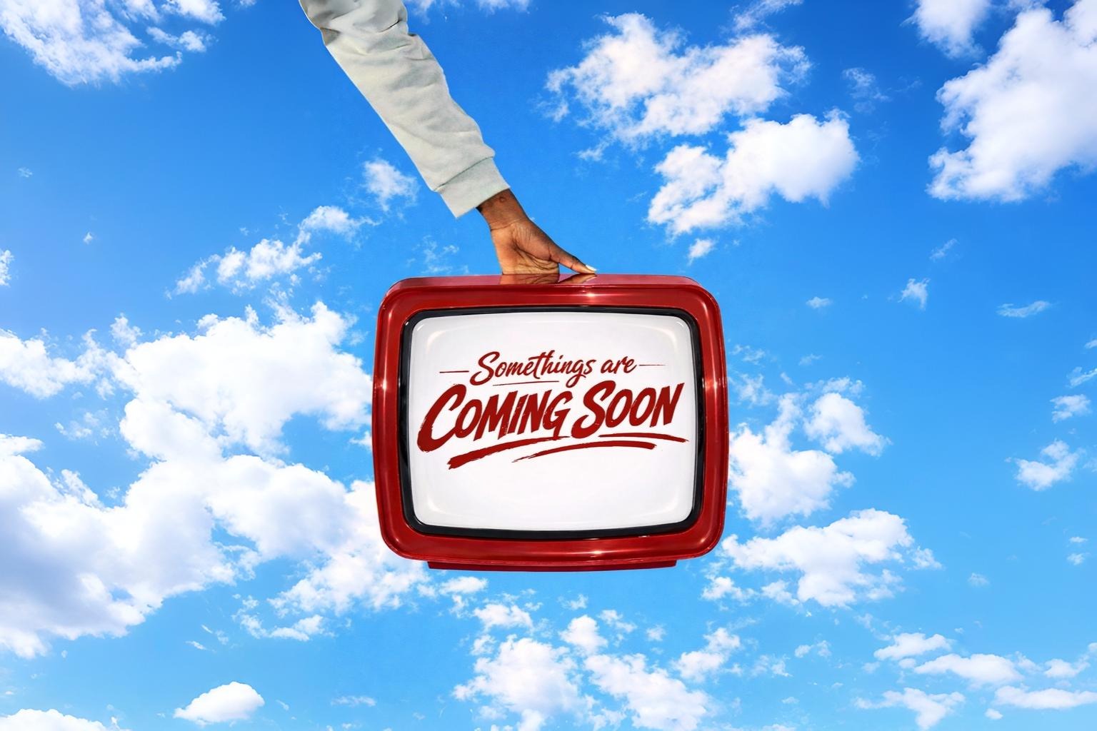A person presents a red and white television with the message "Coming Soon" visible on the screen.