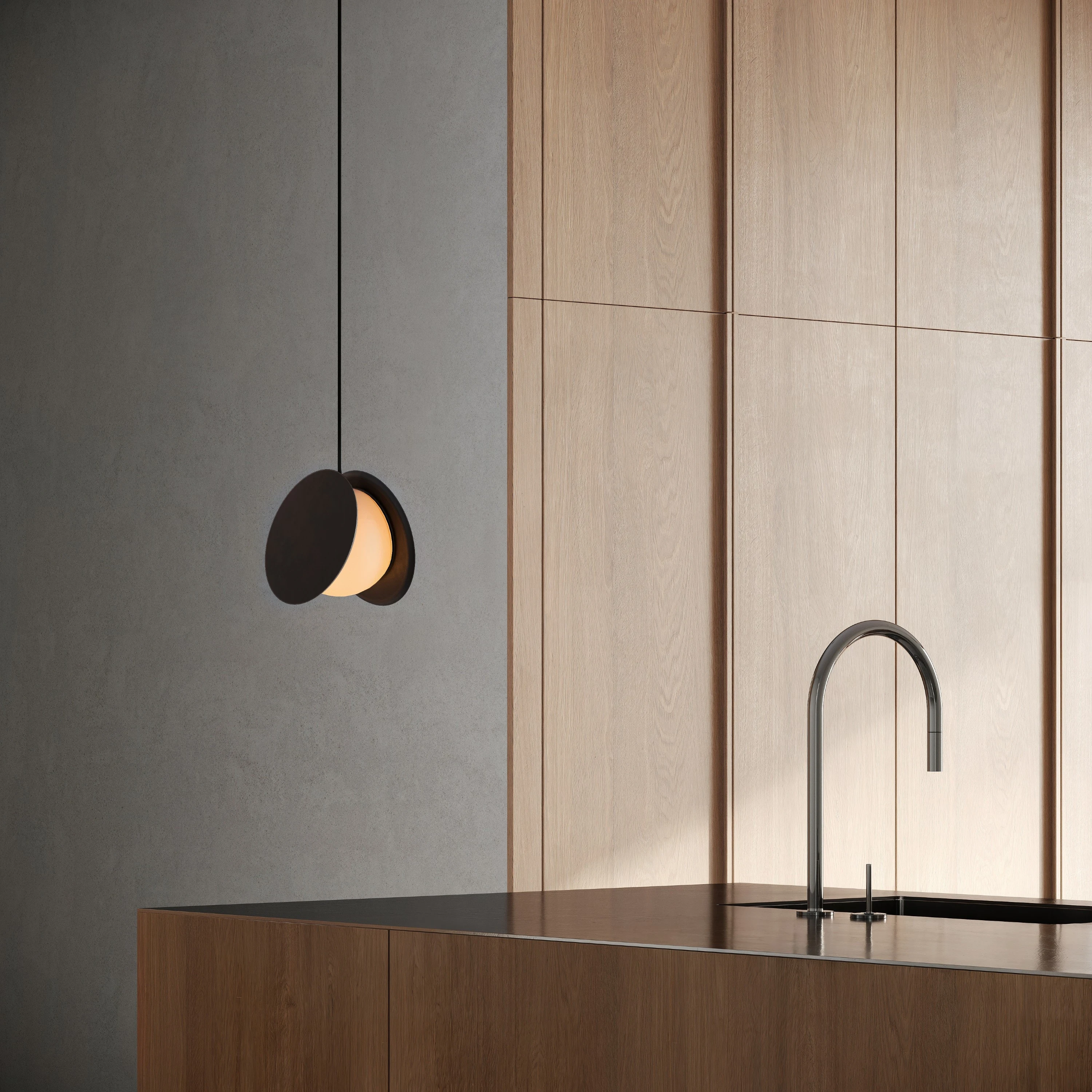 Black pendant light of two offset discs around a glowing globe, hanging over a kitchen island beside wood paneling