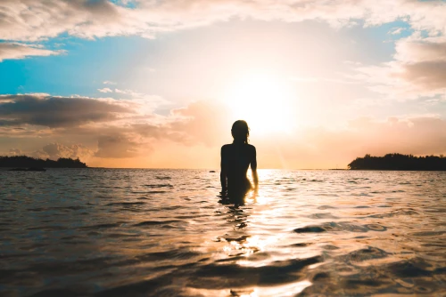 A woman going for a swim while the sun is setting.