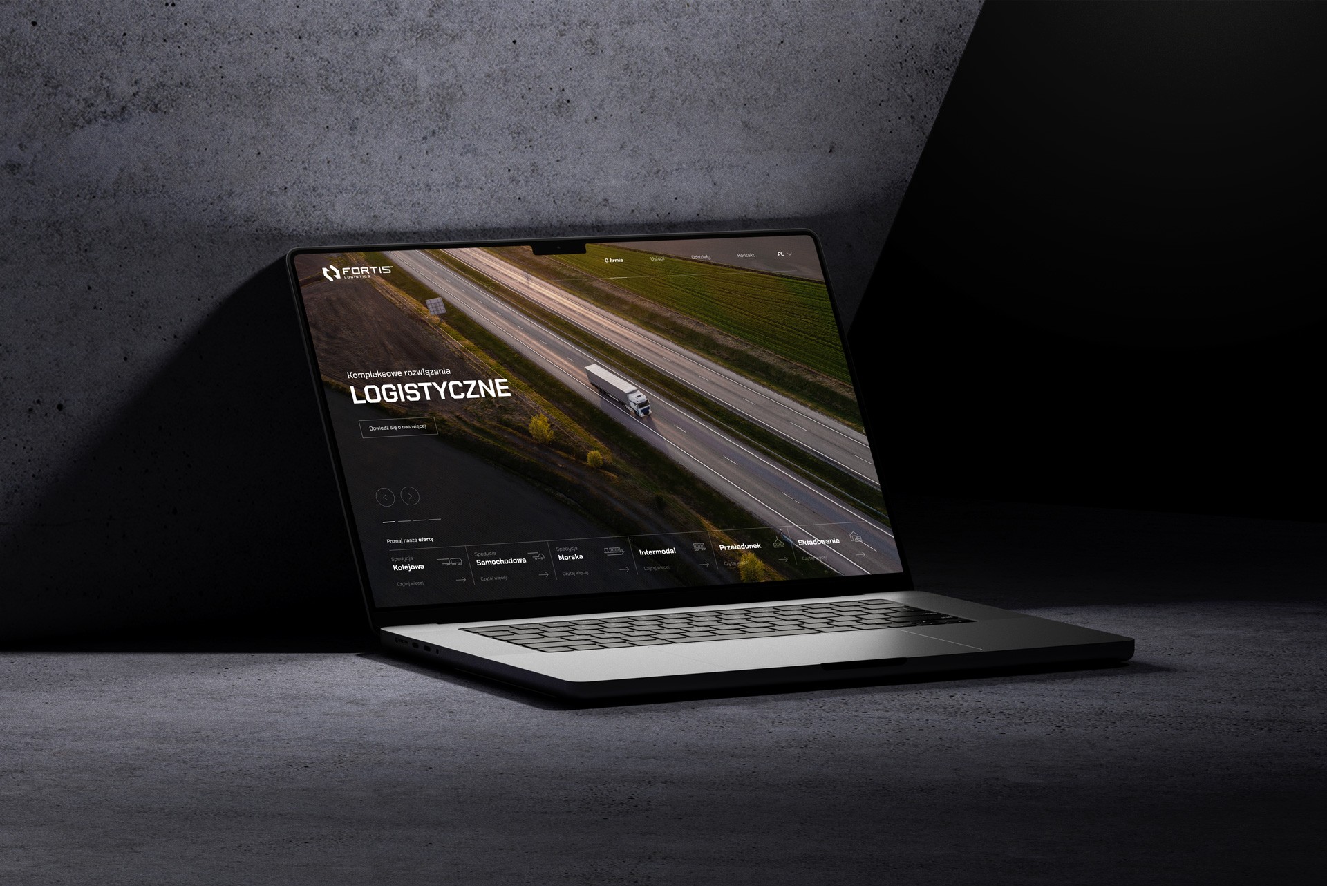A laptop on a dark concrete surface displaying a logistics company website with a highway aerial view and a truck driving on the road.