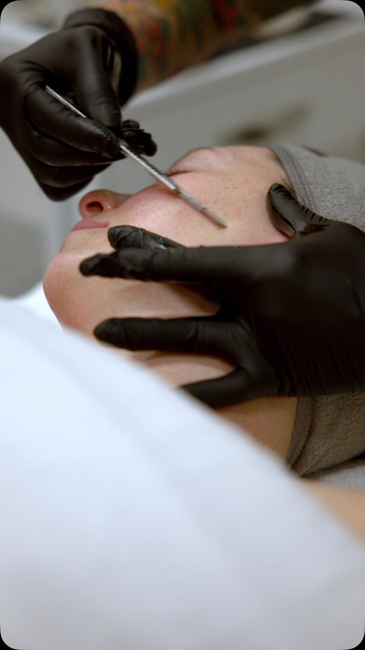 Close-up of Matsuju applying precision skincare with gloved hands during a facial procedure.