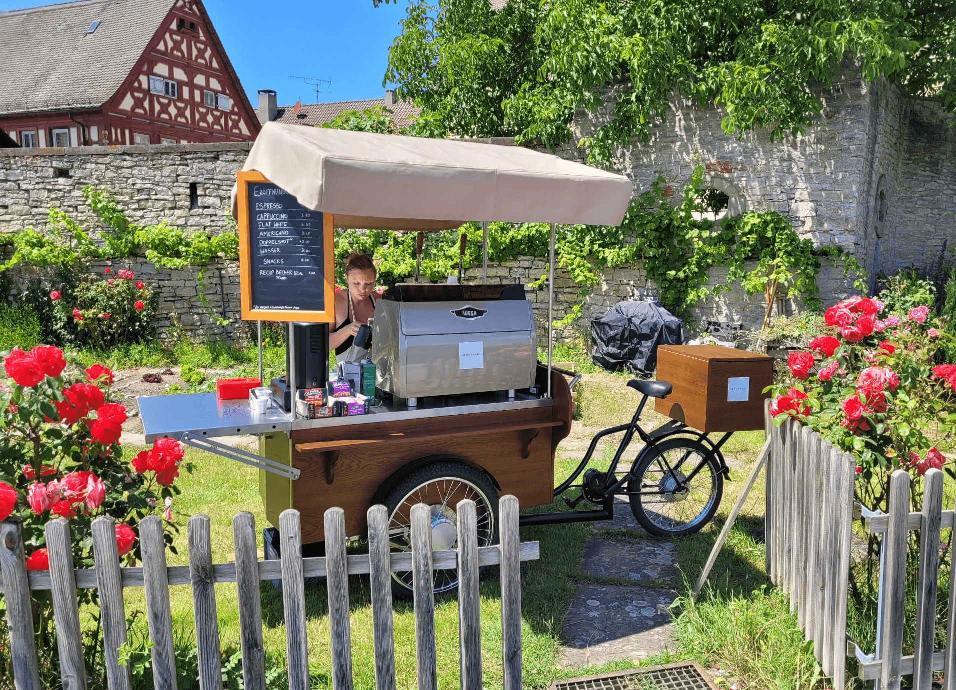 Stilvolles 'Bens Beans' Kaffee-Fahrrad im Grünen, umgeben von Rosen und einem Zaun, perfekt für eure Gartenhochzeit in Sommerach.
