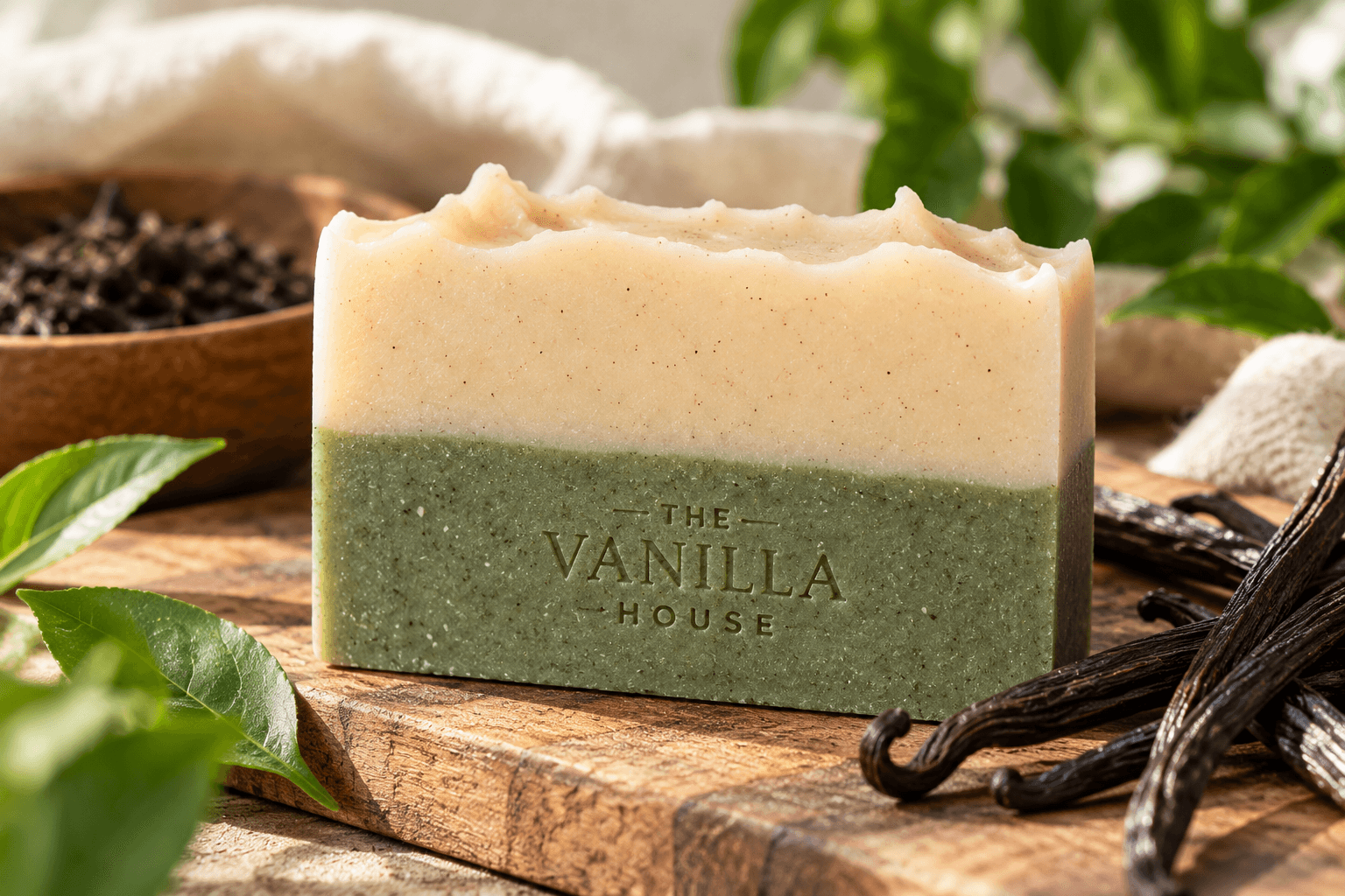 Handcrafted two-tone botanical soap by THE VANILLA HOUSE, featuring a natural cream and muted green finish with delicate vanilla speckles, surrounded by vanilla beans and fresh greenery.