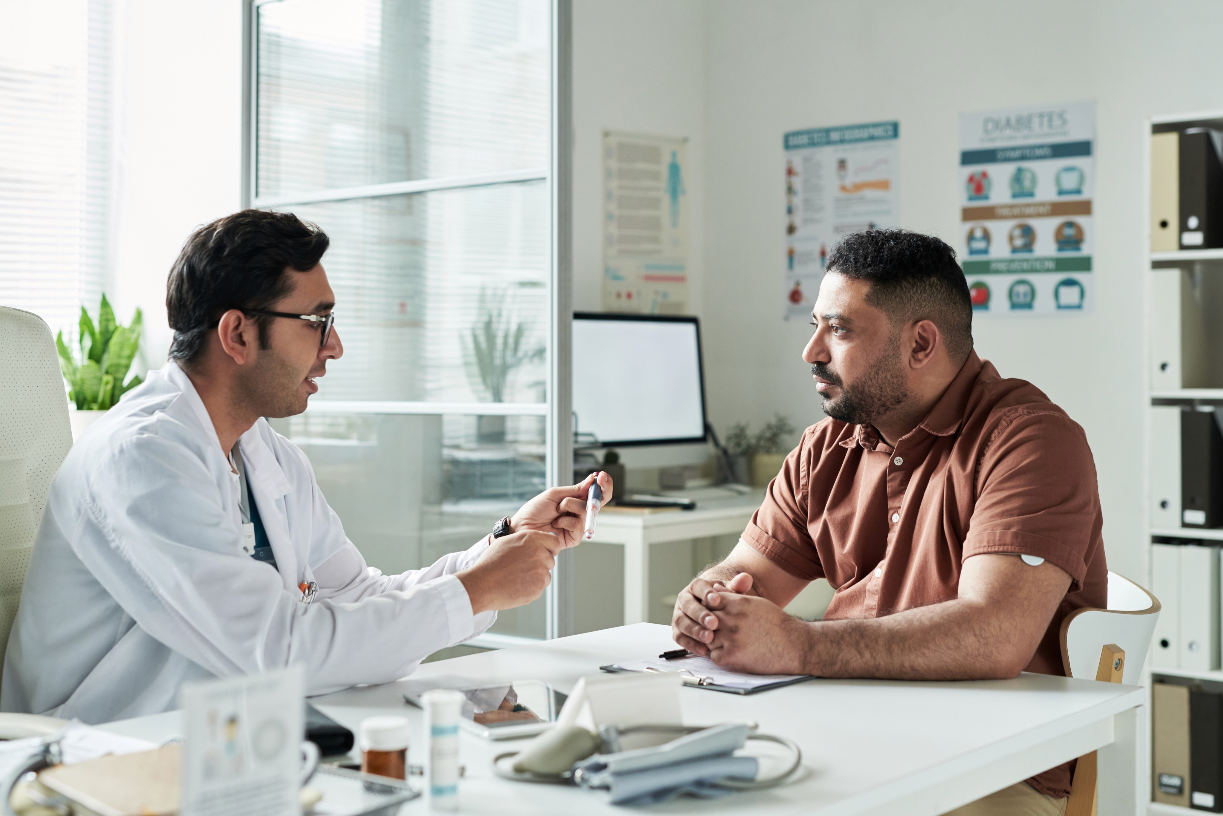 Doctor explaining a blood test result to a patient with medical charts and computer in a bright, modern clinic.