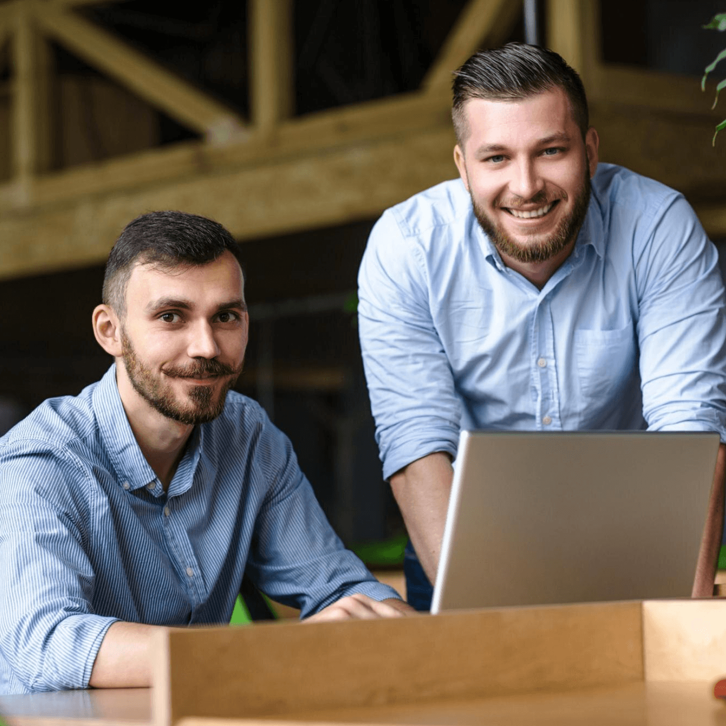 Two people smiling near a laptop in a modern office with wood and plants