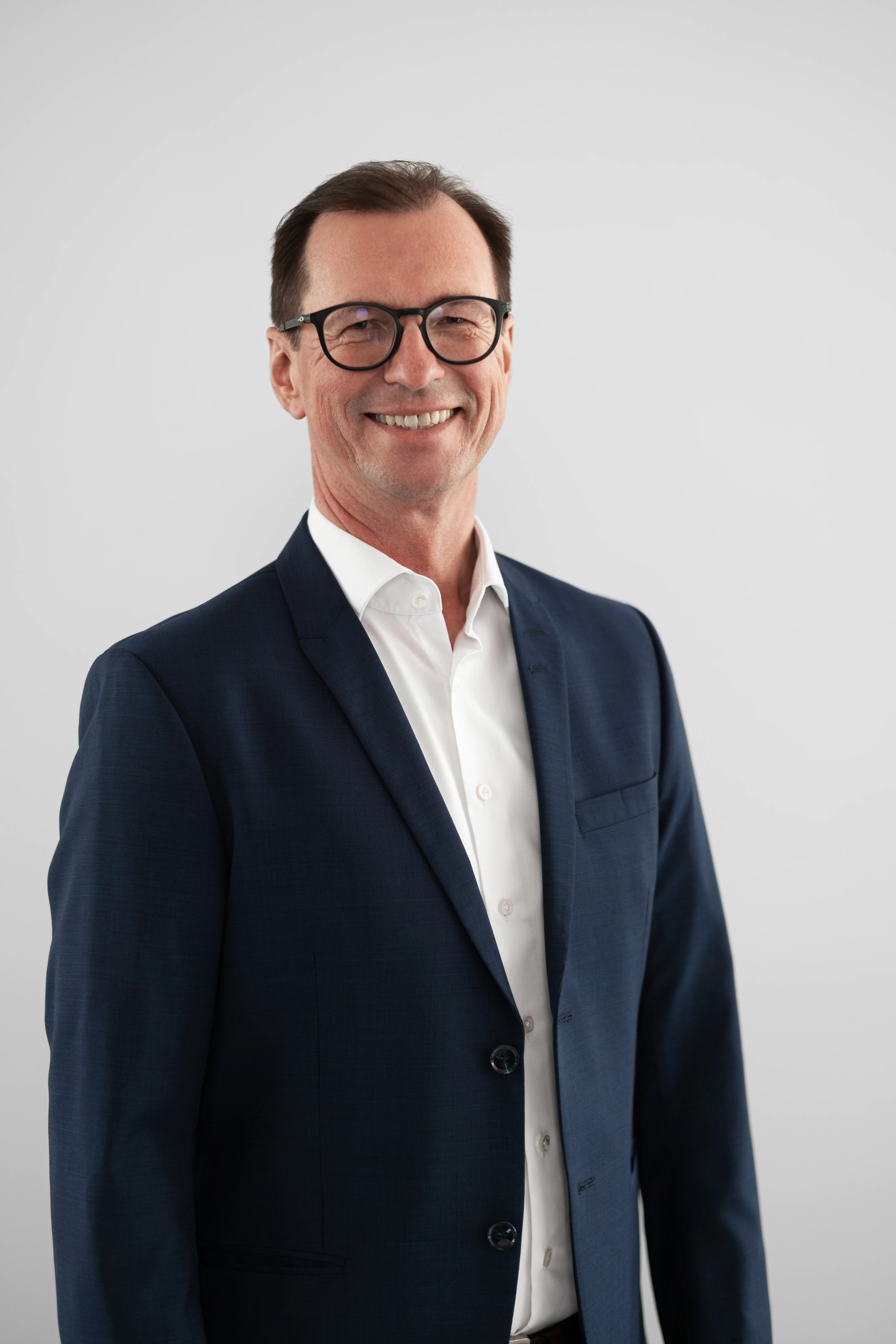 Porträtaufnahme eines professionell gekleideten Mannes mit Brille, der in die Kamera lächelt.
