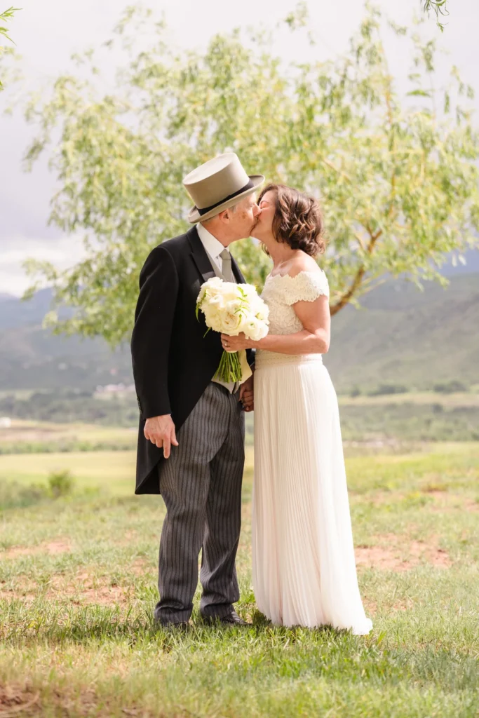 Newlyweds kissing beneath leafy branches in a meadow