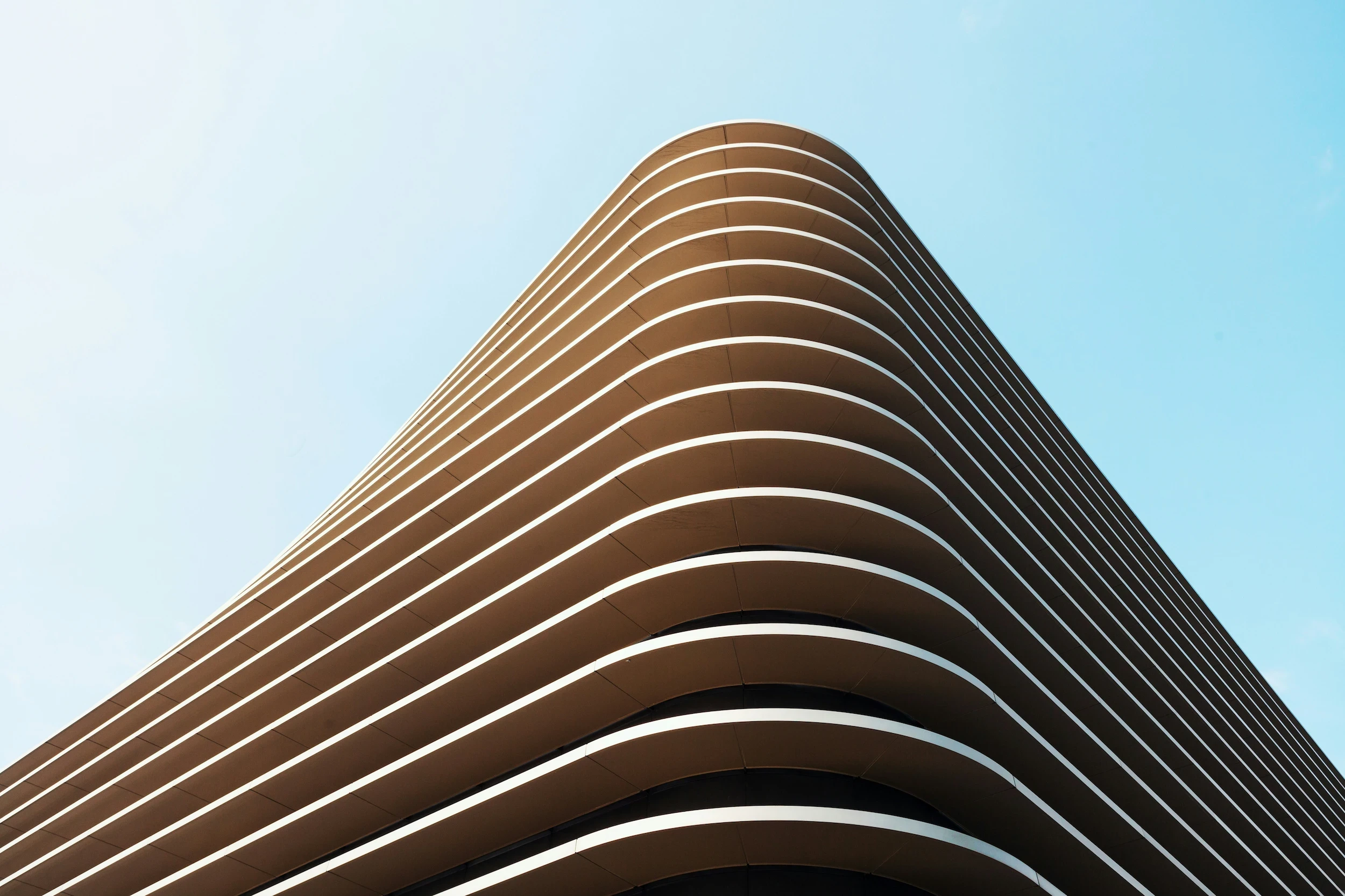 Wide, low-angle perspective of a massive modern building featuring smooth, sweeping white concentric curves and tiered balconies against a clear sky.