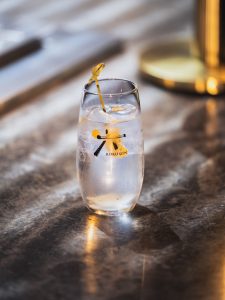 A close-up of a Roku Gin cocktail served in a glass with a garnish, placed on a reflective surface.