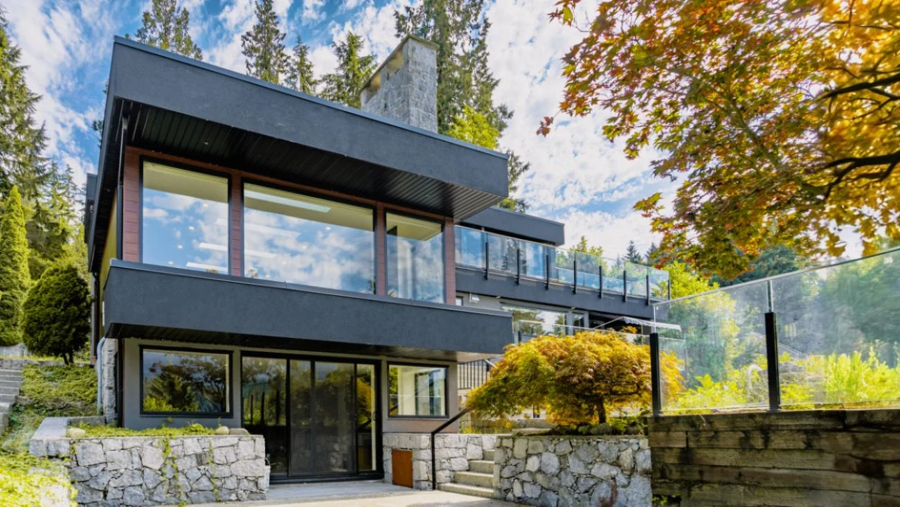 Front exterior view of contemporary custom home with charcoal grey siding, wood accents, large windows, and mature landscaping in Vancouver