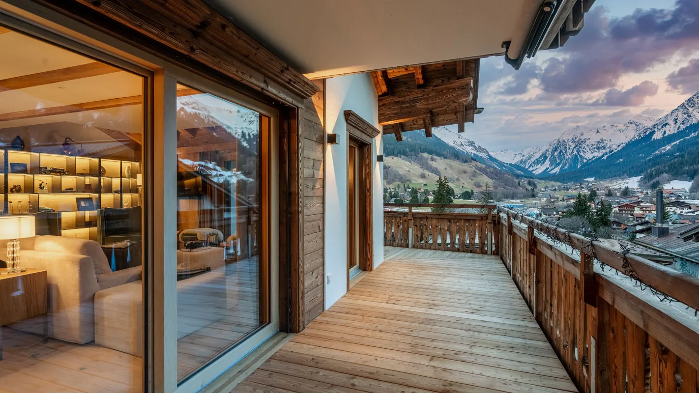 Silvretta Klosters chalet bedroom with exposed timber beams, warm wood joinery, and balcony access