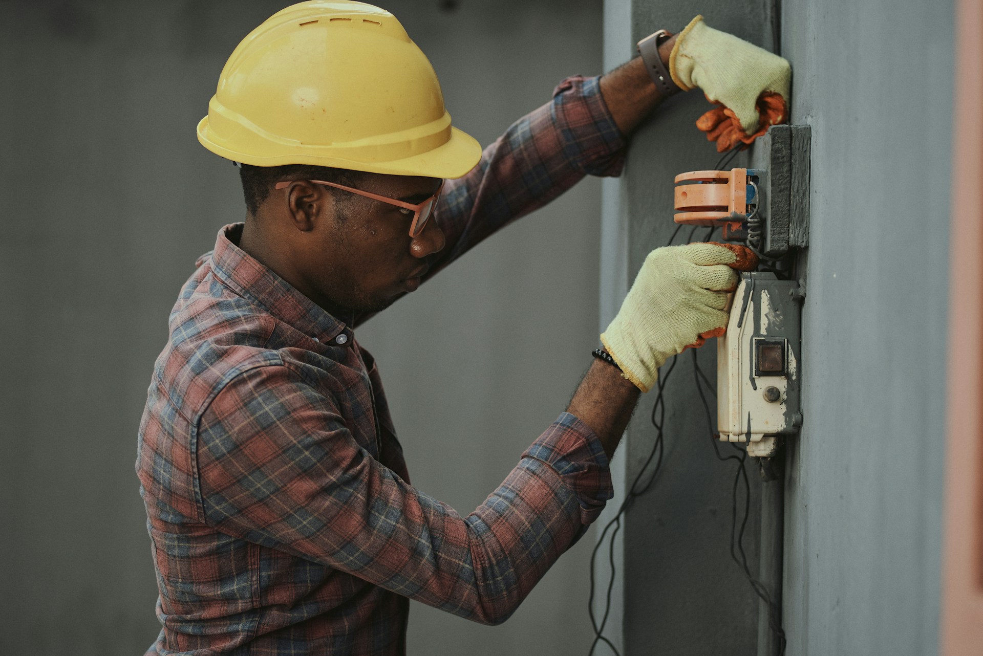 Homme portant un casque jaune et des gants de protection travaillant sur une installation électrique.