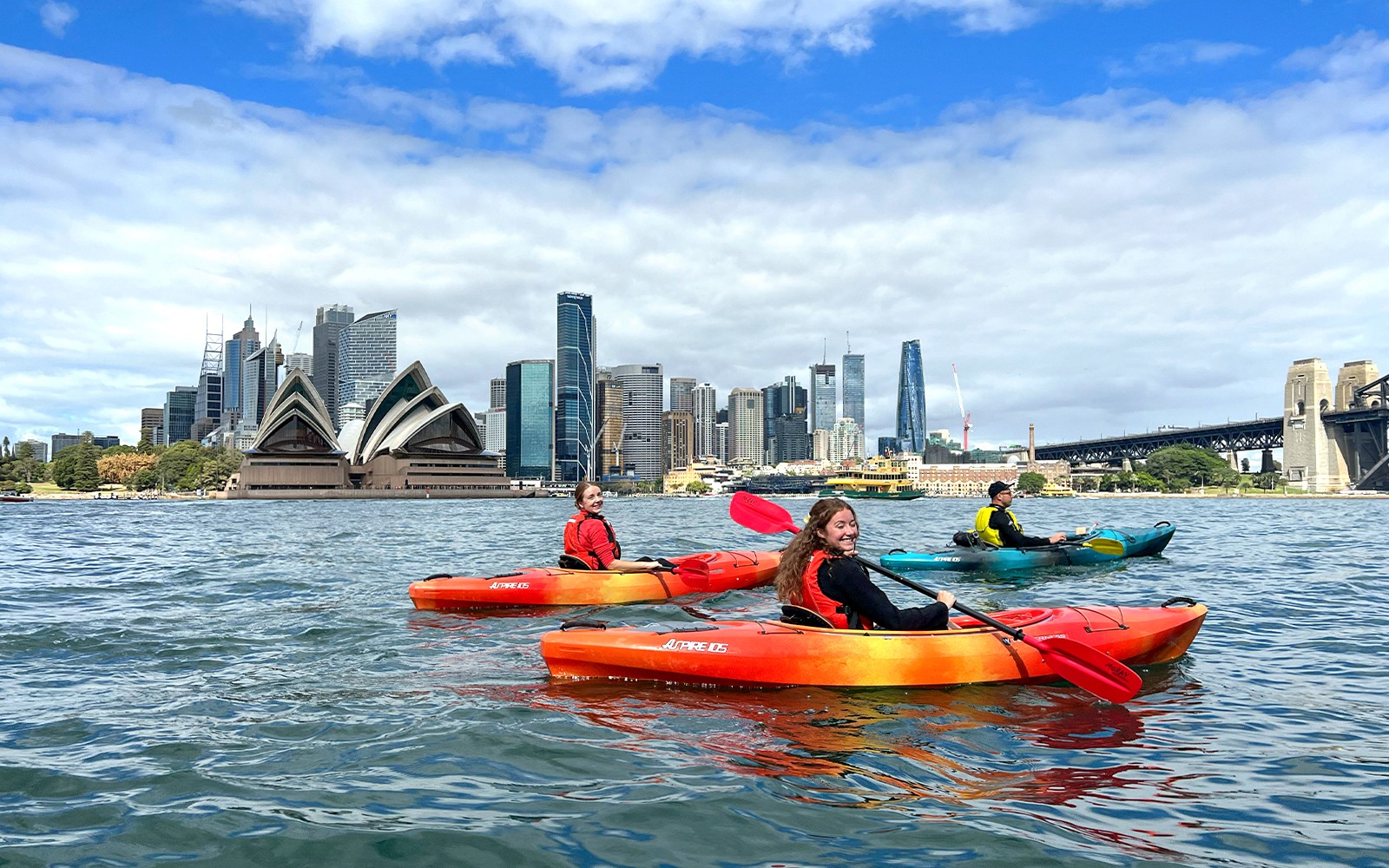 一群人在悉尼港享受皮划艇之旅，背景是著名的悉尼歌剧院，提供可選早餐服務