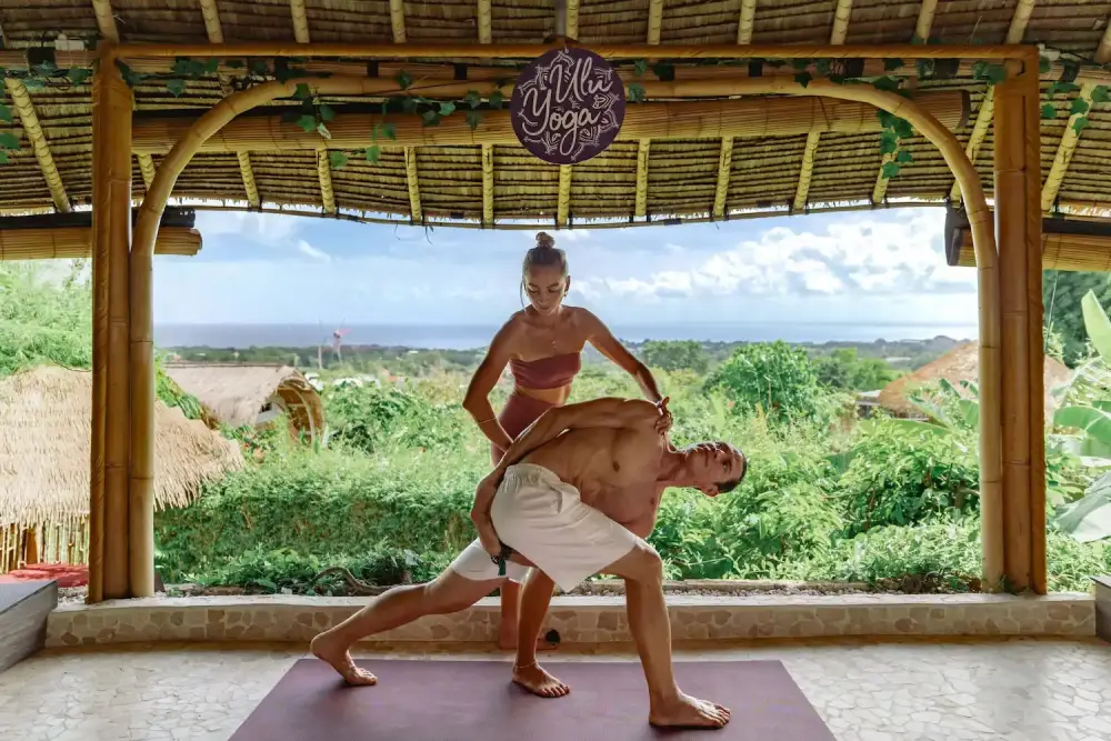 Instructor providing hands-on alignment adjustment to a student during yoga teacher training in the bamboo ocean-view shala.