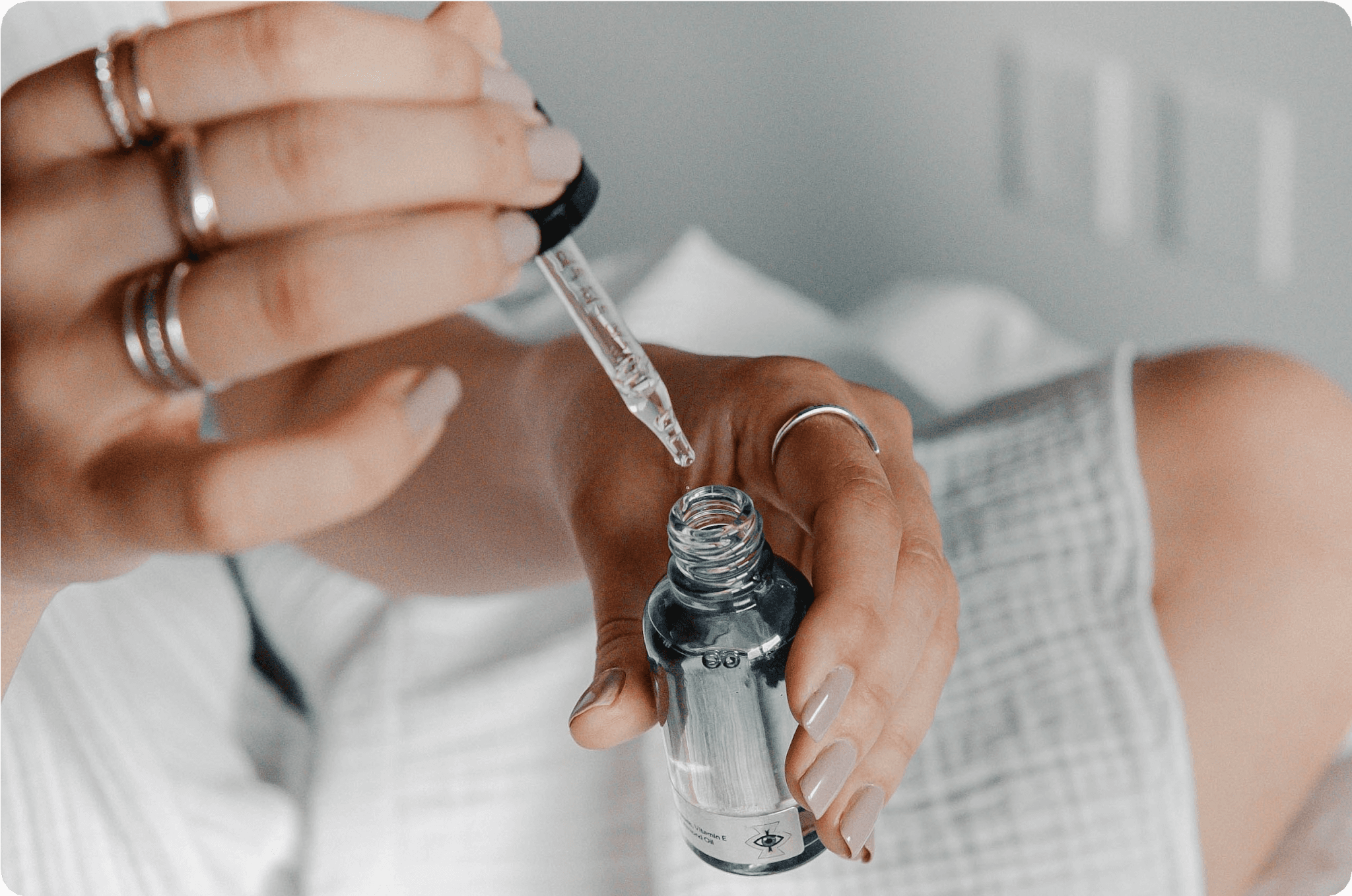 A person using a dropper to apply serum from a glass bottle.