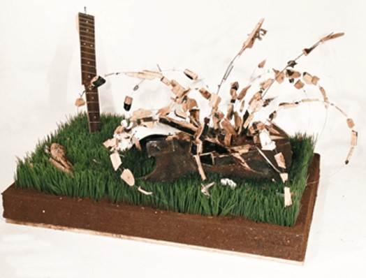 sculpture with grass, an organic shape with rounded structures and a part of an electric guitar