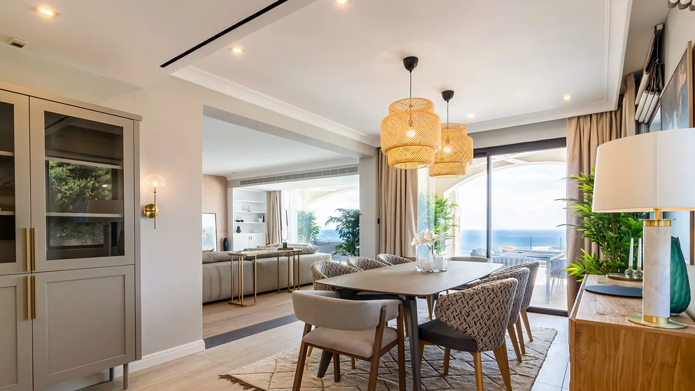 White Cedar House Mediterranean dining area with woven pendant lights and open-plan layout toward sea-view living room