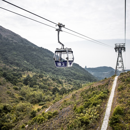 Una funivia viaggia su un terreno collinare e rigoglioso con alberi e montagne sullo sfondo.