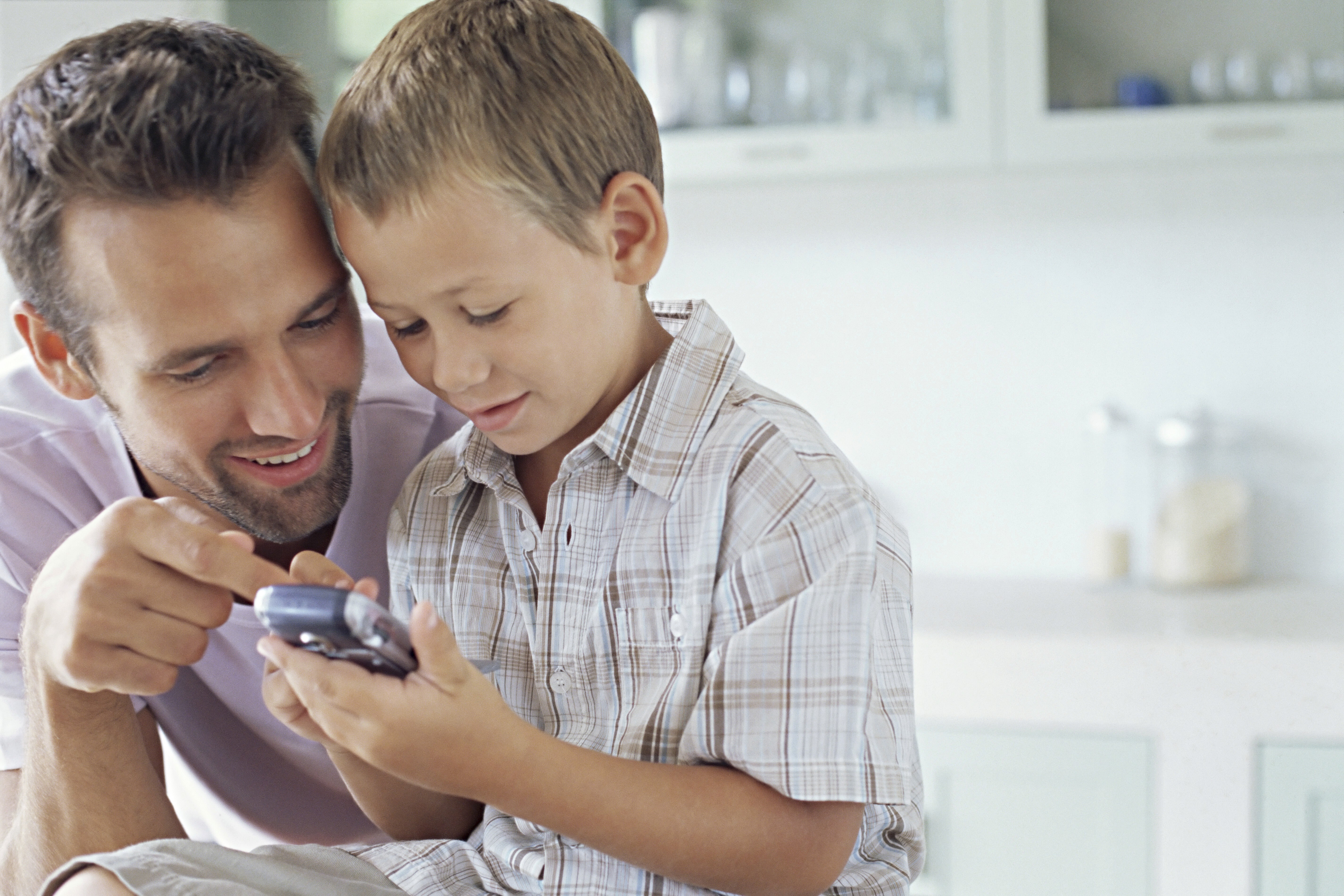 Man wearing an olive green jacket and black shirt, sitting and smiling in front of a light wooden background.