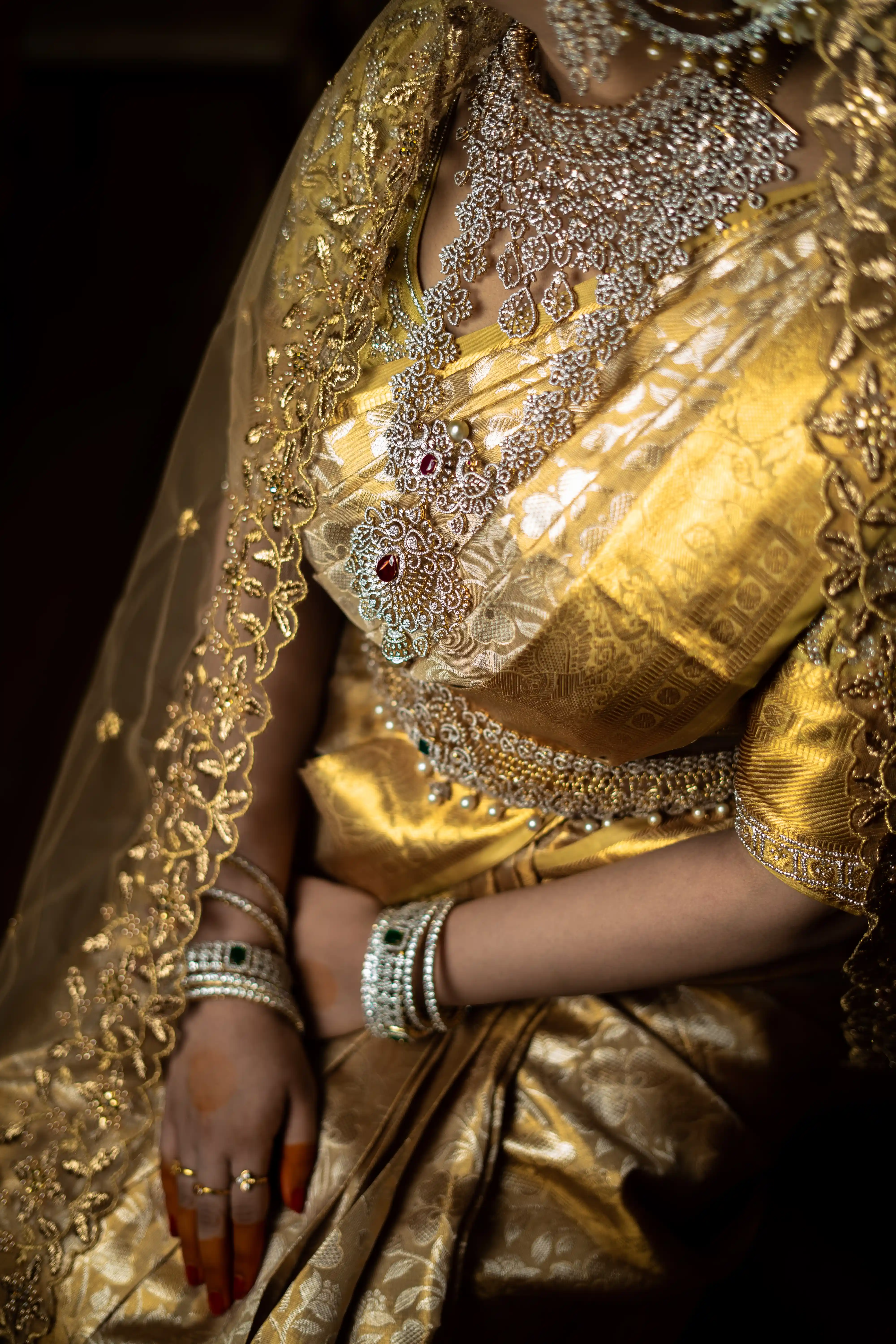 Fine art close-up of a bride dressed in luxurious gold attire and intricate jewelry, with attention to detailed patterns and elegance, captured by Out of The Blues Fine Art Wedding Photography in Hyderabad.