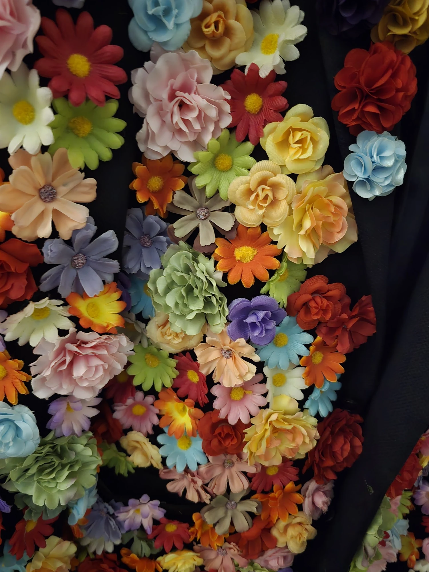 Three-quarter direct-flash study of Le Fleuravelle's black jacket, its lapels and shoulders disappearing beneath layered artificial blooms.