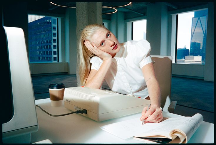 Person resting their head on their hand at a desk with an old computer, looking tired