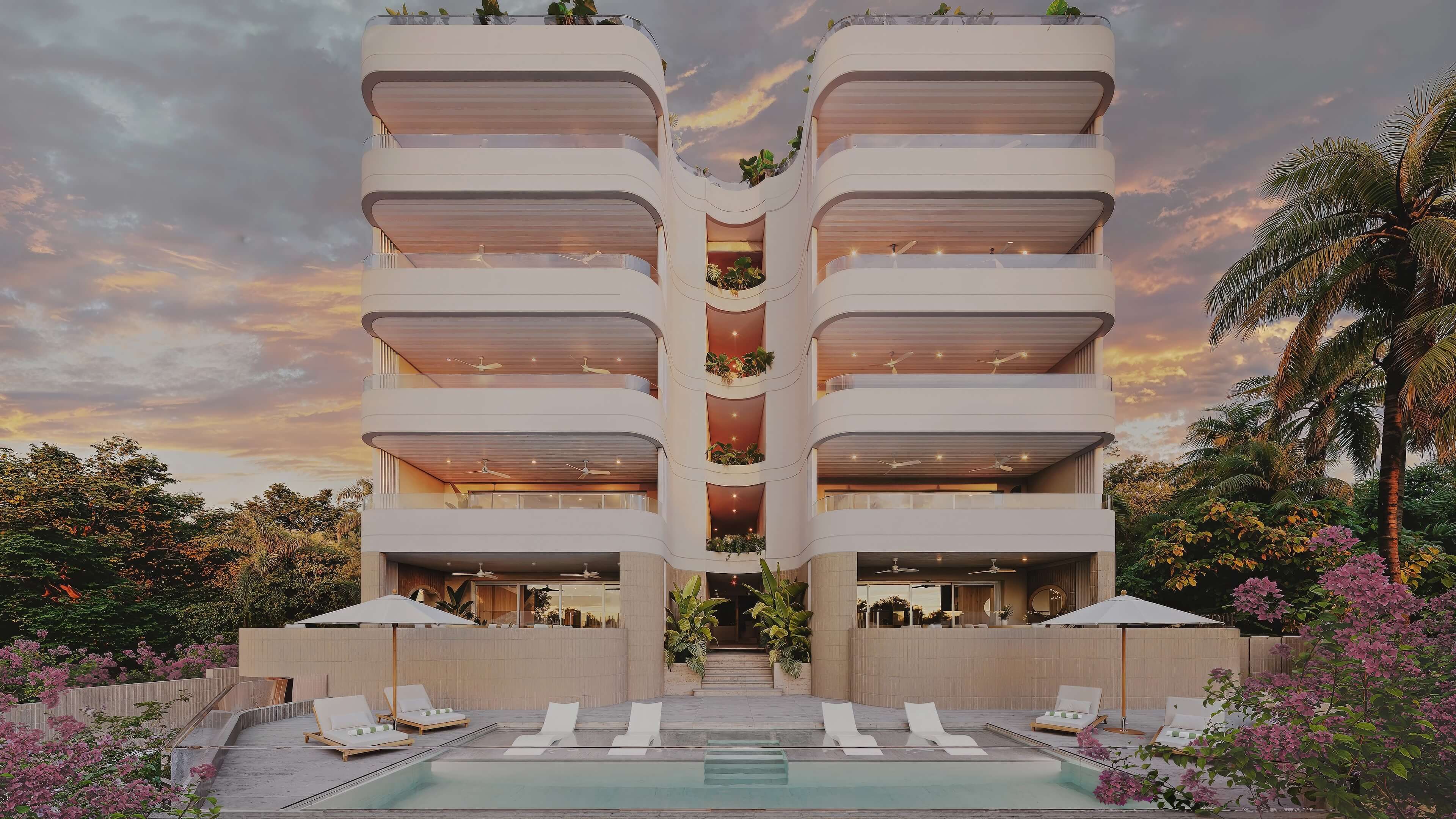 Modern building with a four-story design, surrounded by greenery and a pool, set against a colorful sunset sky.